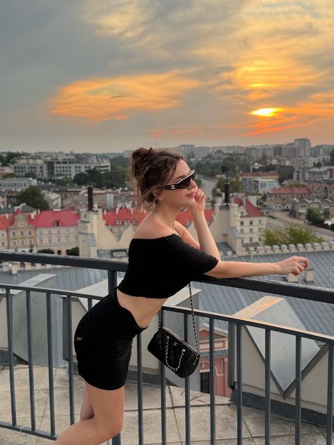 Viki Angels, gün batımında şehri gören bir çatı terasında siyah bir üst ve etekle