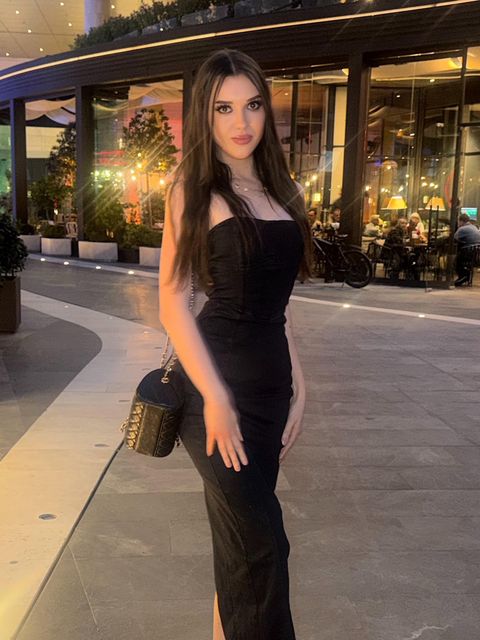 Viki Angels, geceleyin ışıklandırılmış bir restoranın önünde uzun siyah bir elbiseyle