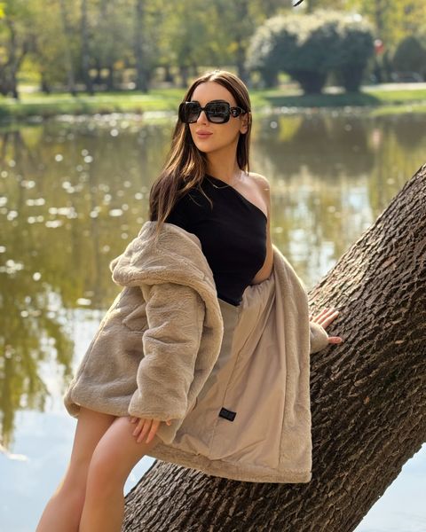 Viki Angels, bir göletin kenarında bir ağaç gövdesinde oturan siyah bir üst ve kürk mantoyla